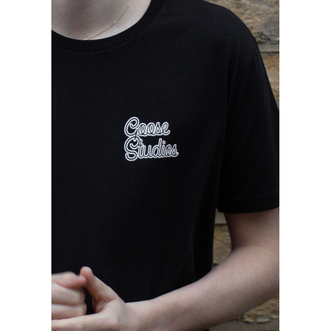 Close up of man wearing black short sleeve organic cotton t-shirt with white Goose Studios logo on left chest